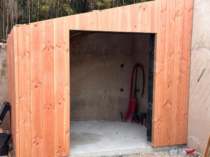 Construction d'un cabanon de jardin sur mesure en ossature bois, habillé d'un bardage vertical en Douglas, servant de local technique pour piscine.